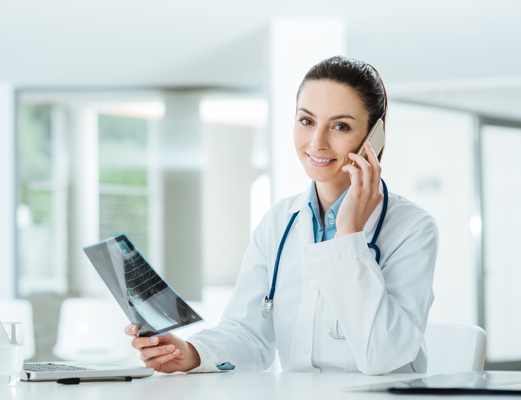Smiling female doctor on the phone in the office holding medical records and talking with a patient
